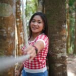 A cheerful woman in a red checkered shirt enjoys a sunny day in the forest.