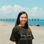 Asian woman smiling on beach with Boracay Island t-shirt and pier in background.