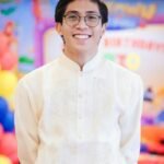 Young man in traditional Filipino attire smiling at a colorful indoor event setting.